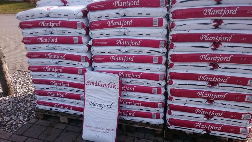 Staplar av vita och röda Plantjord Småländsk 50L-påsar på träpallar utomhus.