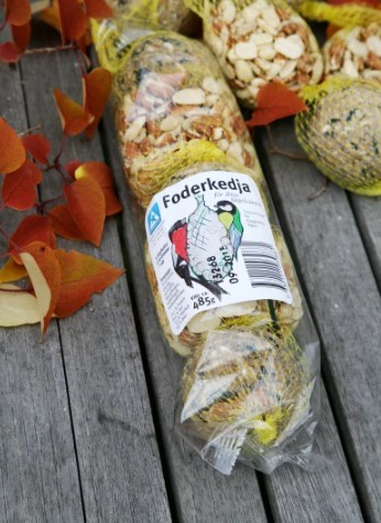 Foderkedja 485g fågelfoderkedja i gult nät på bord med höstlöv, svensk etikett visas.