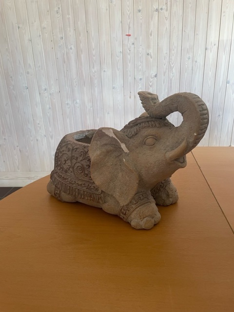 En dekorativ elefantstatyett i sten på ett träbord med en bakgrund av ljus träpanel.