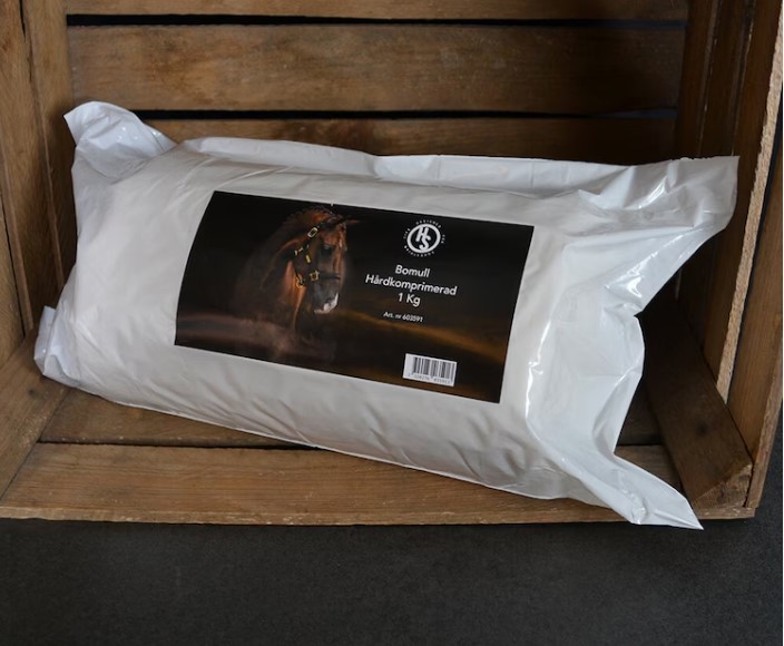 I en trälåda vilar en vit förpackning med Bomull Hårdkomprimerad 1kg.