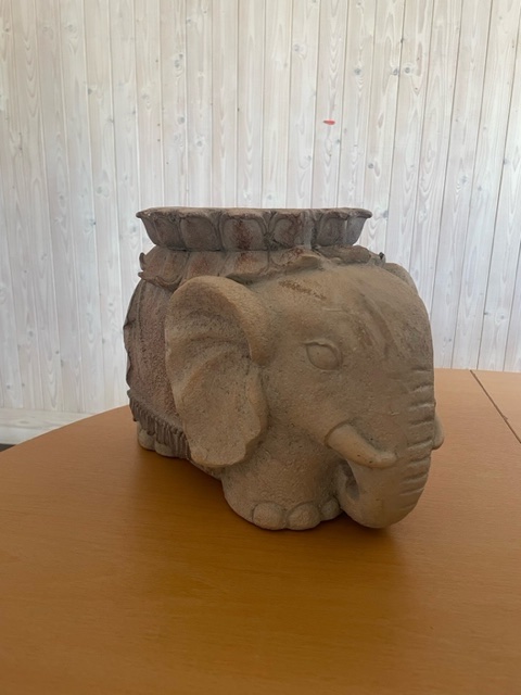 Elefantformad planteringskärl av sten på ett träbord med en ljus träpanelvägg i bakgrunden.