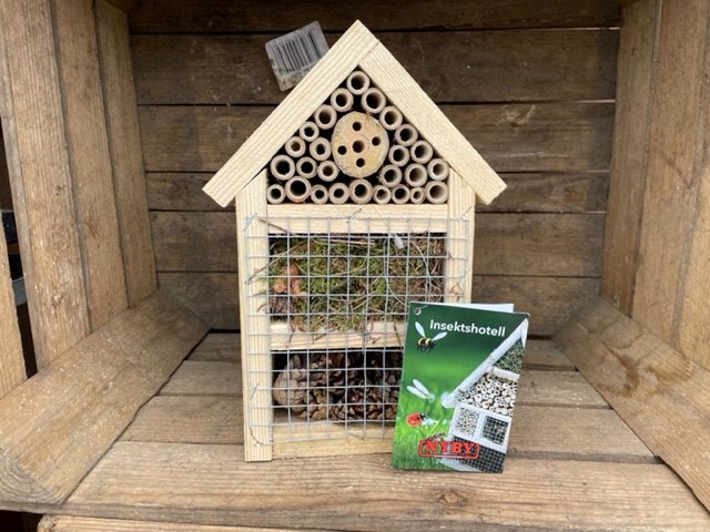 Insektshotell insektshotell med rör och nät, utställda på en trähylla med frontetikett.