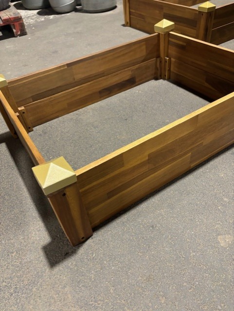 Odlingskrage 75x55x24 upphöjd sängram i trä med guldlock på betonggolv.