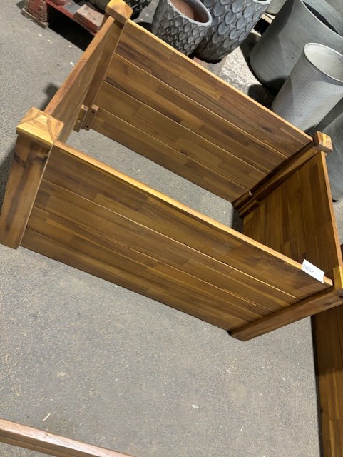 Träplanteringen Odlingskrage 78x58x44 står på ett betonggolv med fler planteringar bakom.