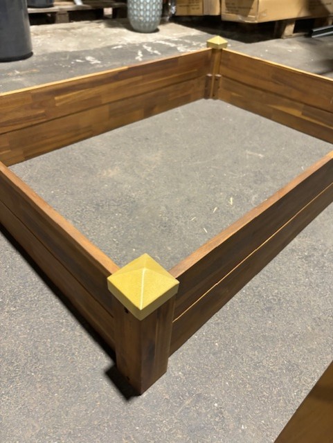 En rektangulär lådram av trä med guldkapslade hörnstolpar på en arbetsbänk.