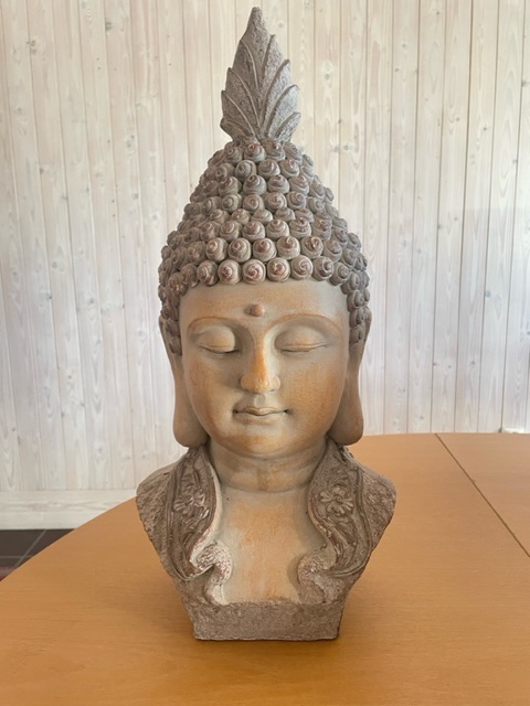 Buddha-huvudstaty i sten på ett träbord med en bakgrund av ljus träpanel.