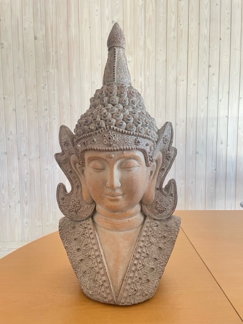 En Buddhastaty i sten på ett träbord med en bakgrund av ljus träpanel.