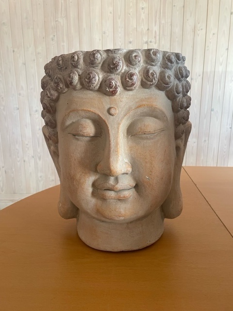 En keramisk kruka med Buddhahuvud på ett träbord med en bakgrund av ljus träpanel.