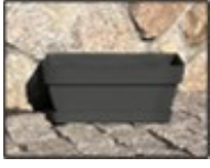 En Rektangulär plastkruka m fett sitter på stenbeläggning mot en stenmur.