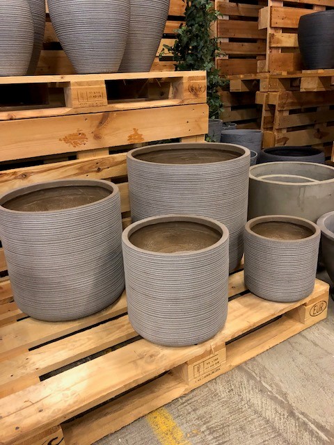 Fyra Kruka fiber grå - XL växtkrukor på träpallar i en butik.