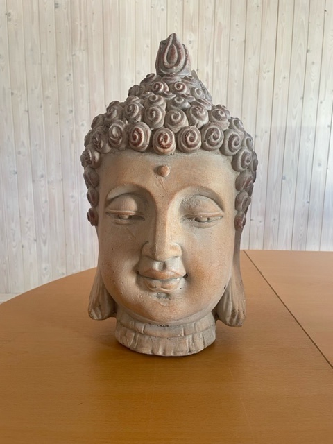 Buddha-huvudstaty i sten på ett träbord med en bakgrund av ljus träpanel.