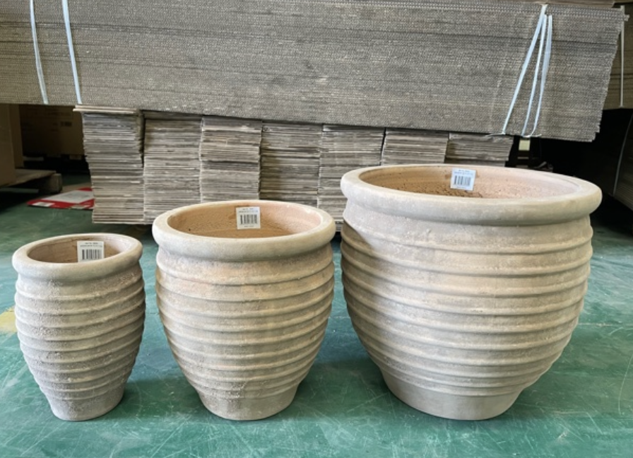 Stor beige ribbad antik terra växtkruka framför staplad kartong.