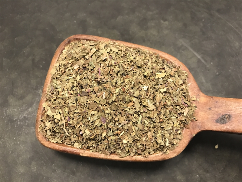 En träskopa fylld med BASILIKA (20 g) torkade örter på en mörk yta.