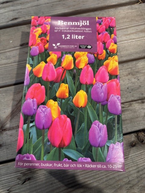 En låda KRAV Benmjöl NP7-9 1,2L gödselmedel med tulpaner på locket står på en träbit.