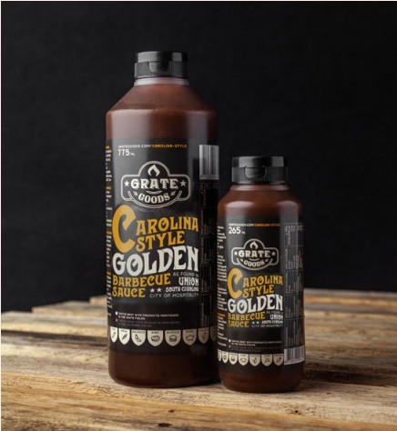Två flaskor Carolina Golden Barbecue Sauce på en träyta med svart bakgrund.
