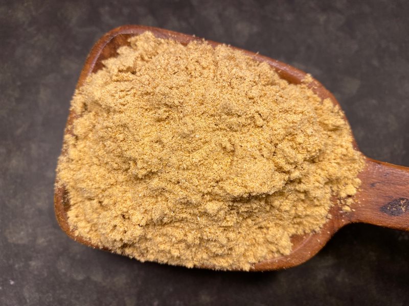 En träsked med Curry Mango-pulver mot en mörk bakgrund.