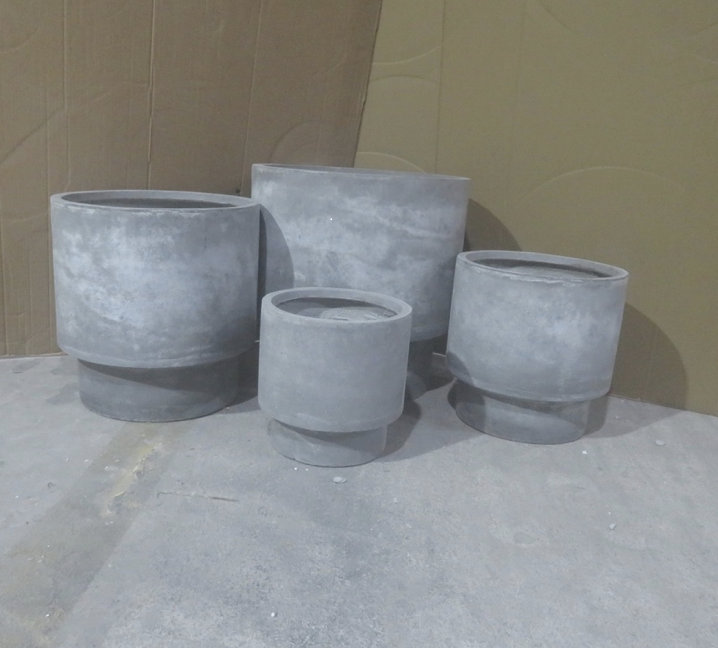 XL grå fiberplantering på betonggolv mot en brun vägg.