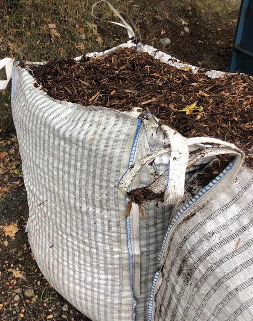 Flis/ Bark, storsäck 1m3: Stor vit vävd säck med barkflis, delvis sönderriven upptill.