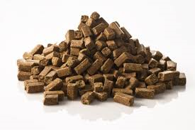 En hög med bruna, rektangulära djurfoderbitar mot en vit bakgrund.