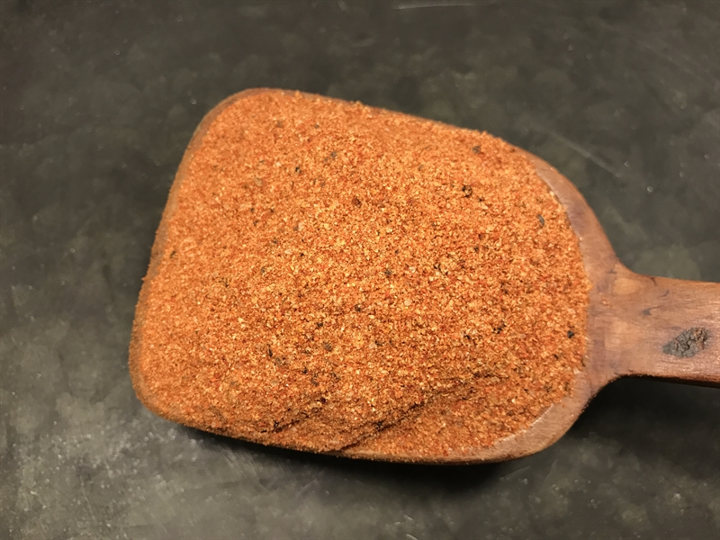 En träskopa med Grillkrydda Honung-krydda vilar på en mörk yta.