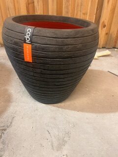 Stor svart räfflad kruka KRUKA CAPI SVART med orange tagg på ett betonggolv.