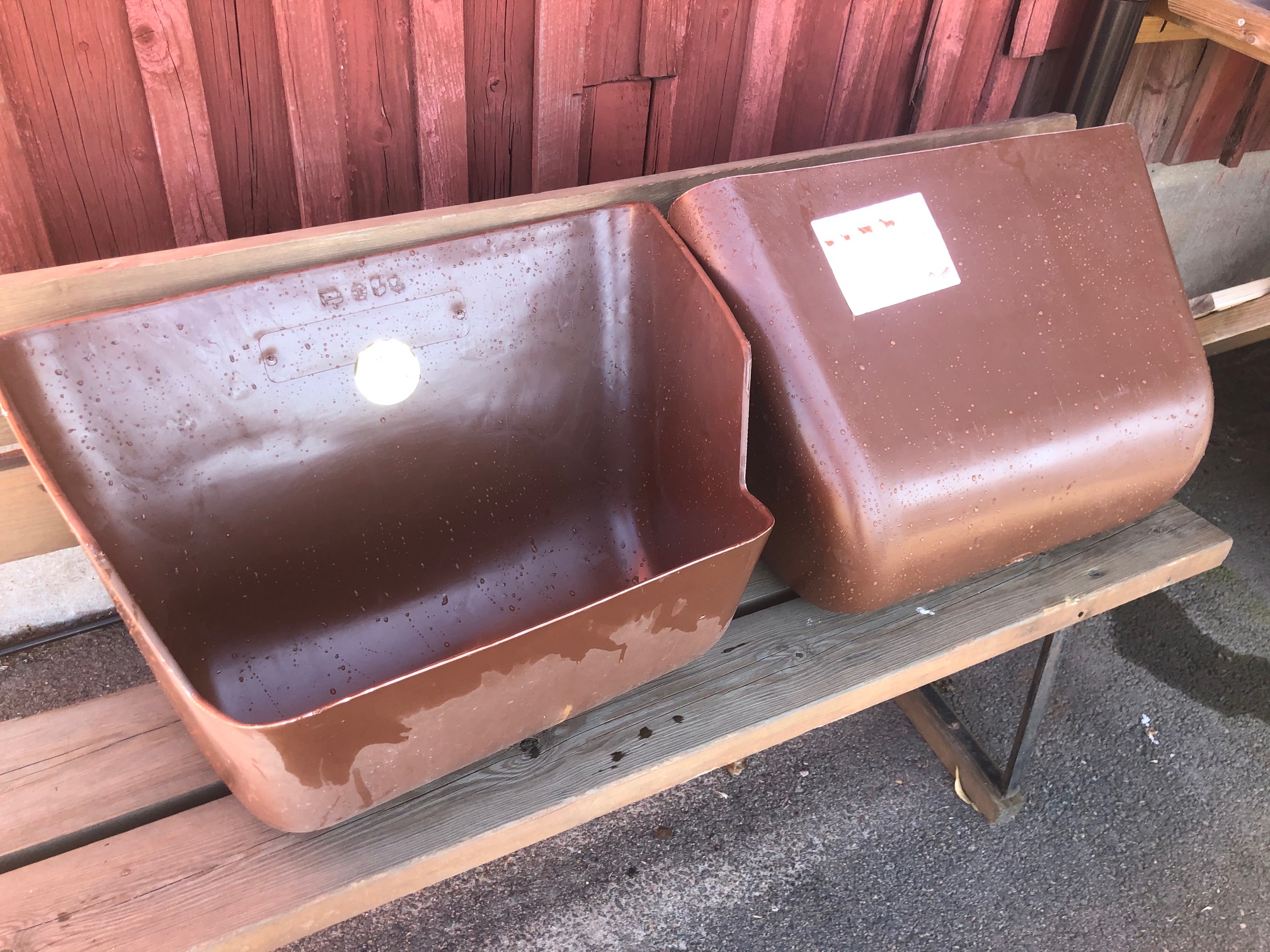 Två stora Foder krubba-kärl på en träbänk utanför vid en röd vägg.