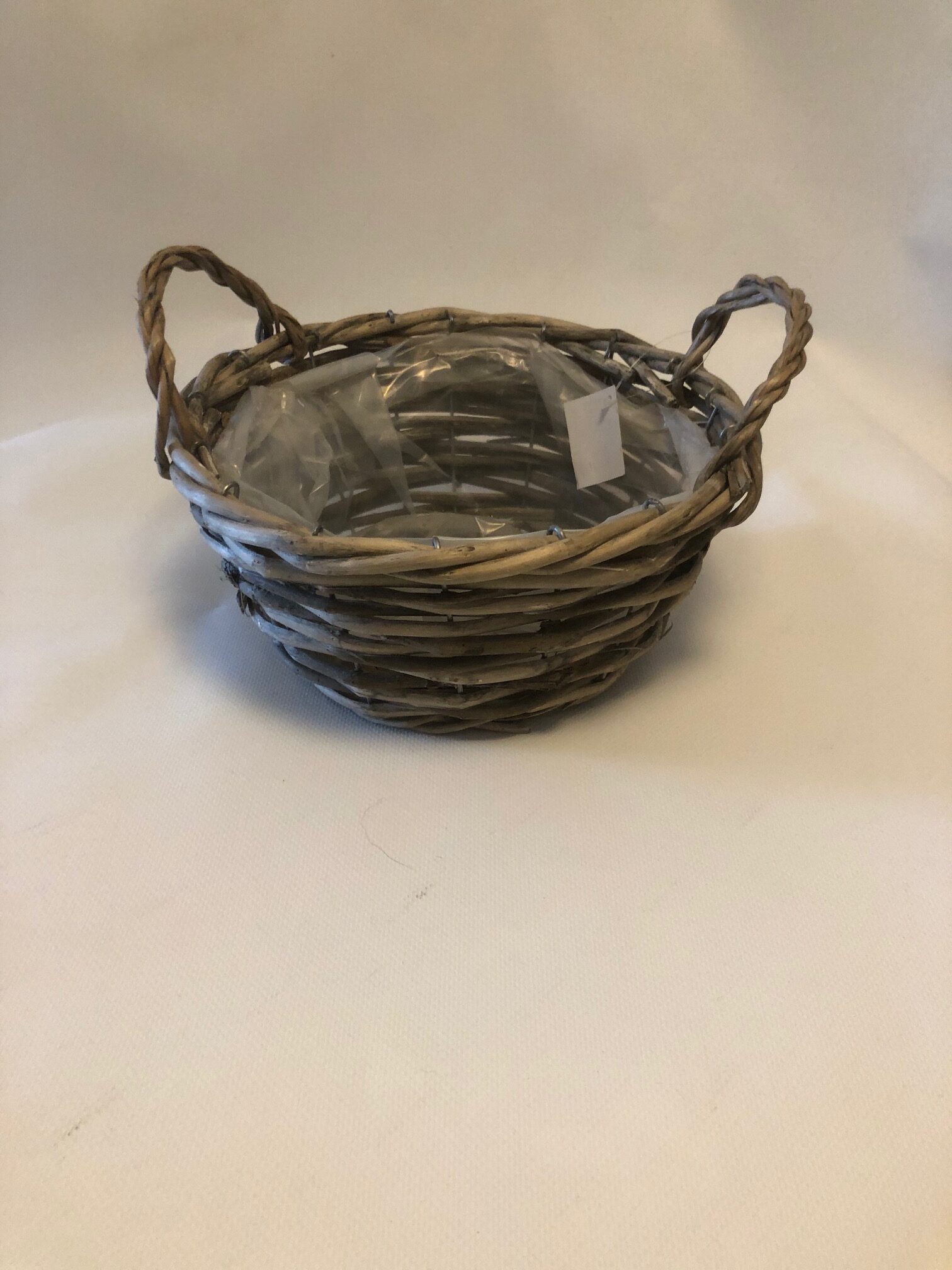 Korg grå rund D23 korg med två handtag, fodrad med genomskinlig plast, mot enfärgad bakgrund.