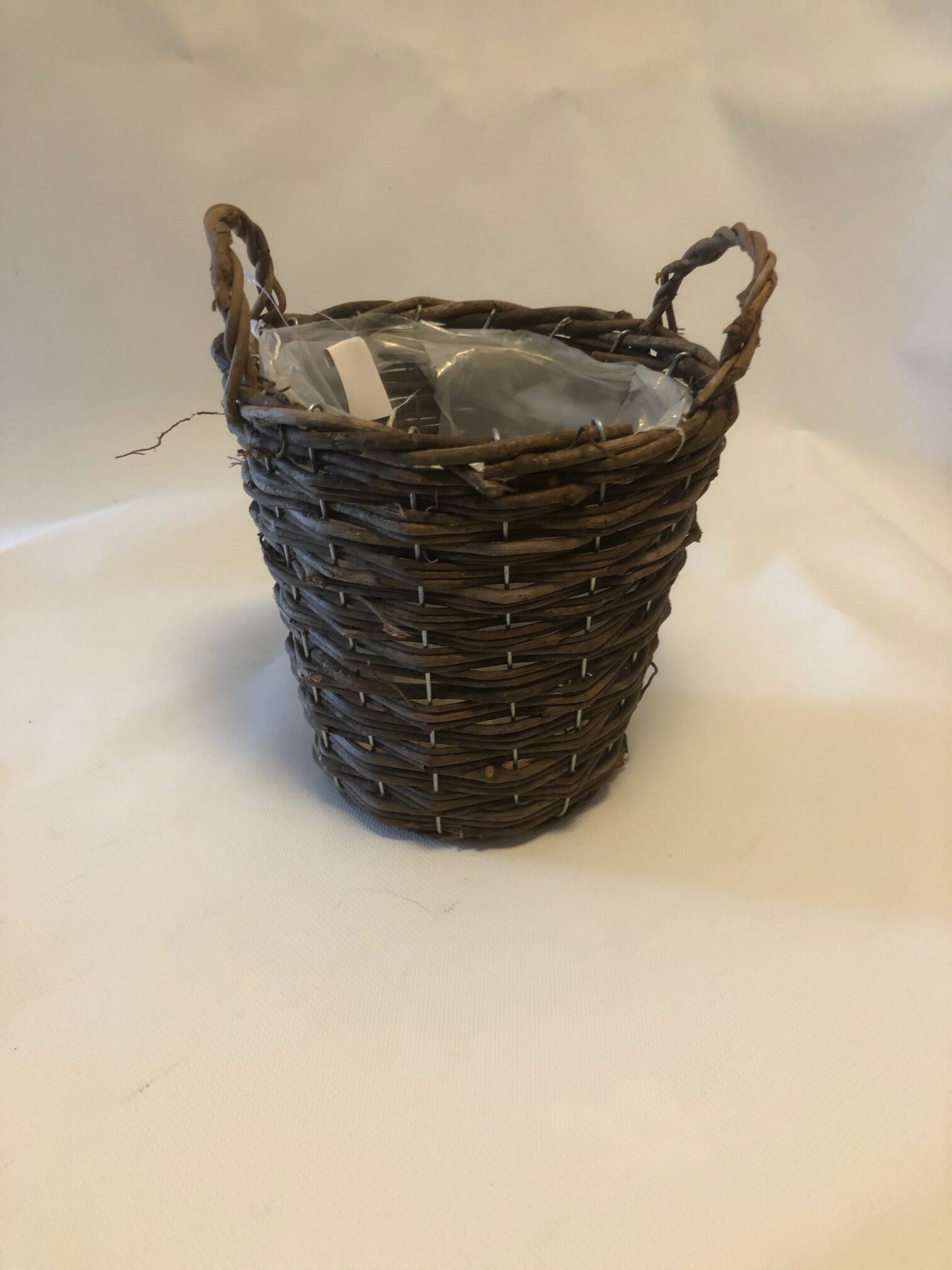 Korg Natur D19 korg med handtag håller ett plastförpackat föremål mot en slät bakgrund.