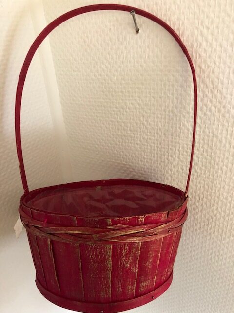 En Röd korg i trä med handtag hänger på en strukturerad vit vägg.