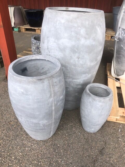 Tre stora Urna grå - H88 betongkrukor i varierande storlekar på pall utomhus.