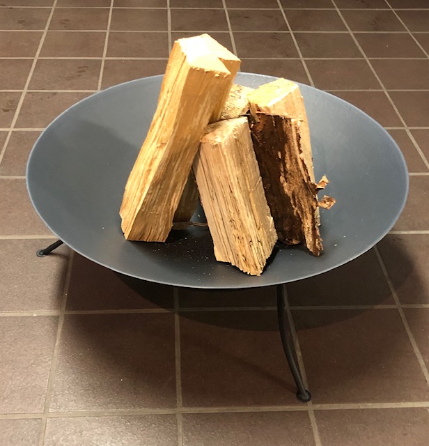 Eldfat D61 cm svart eldstad rymmer staplad ved på ett brunt klinkergolv.