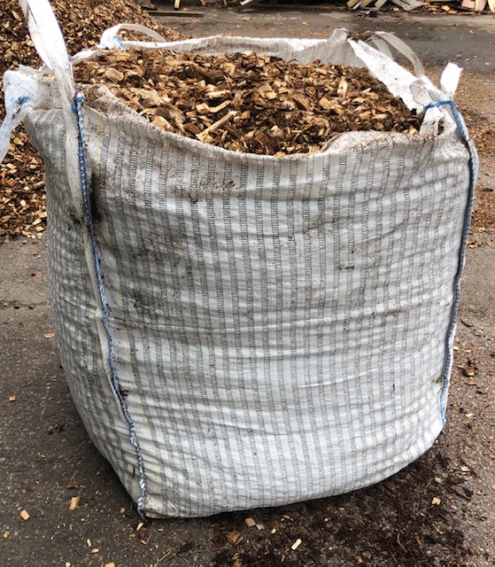 Stor vit säck fylld med träflis, stående på en asfalterad yta utomhus.