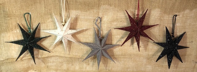 Fem Pappersstjärna 20 cm prydnadsföremål hänger på rad mot en bakgrund av säckväv.