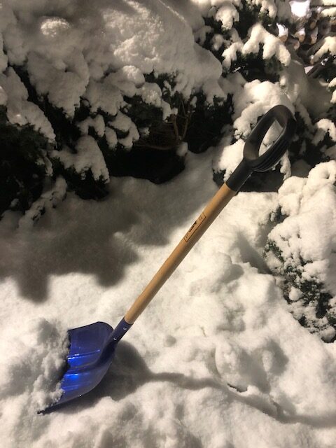 Snöskyffeln Karlstad, blå, står upprätt i djup snö bland snötäckta buskar.