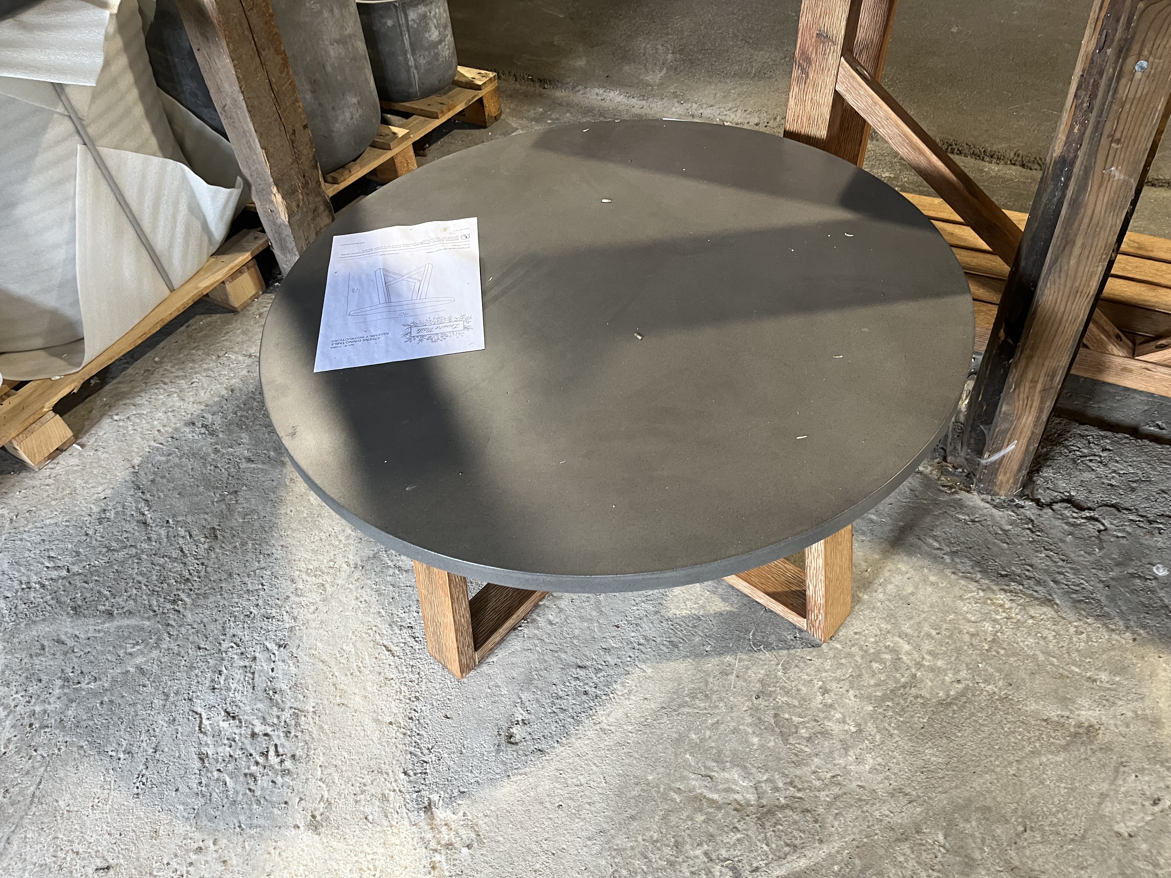 Runt lågt bord: rund mörk bordsskiva, träben, papper på toppen, i en lagerlokal.