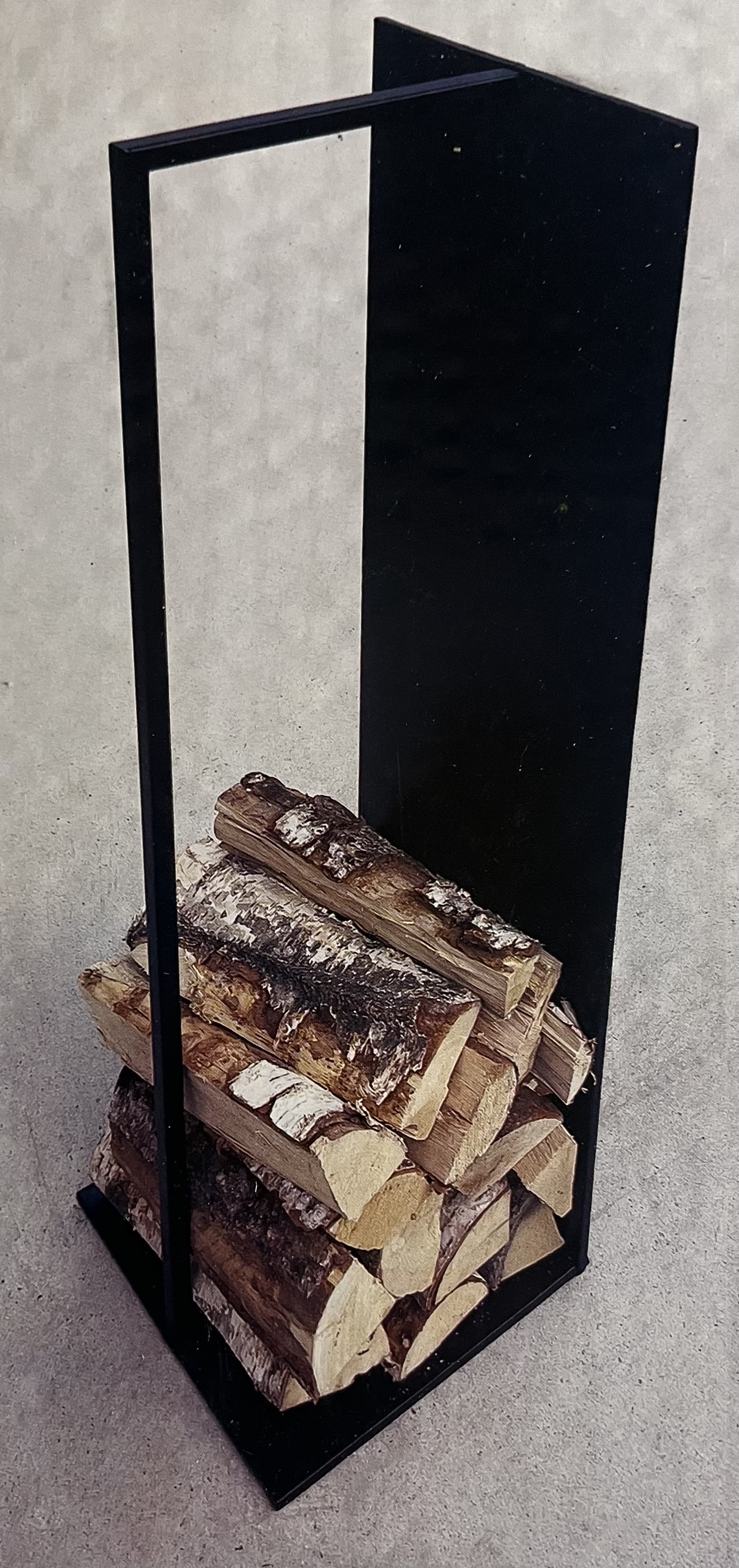 Staplad ved i vedställ 100X30X30 svart metallhållare på grått golv.