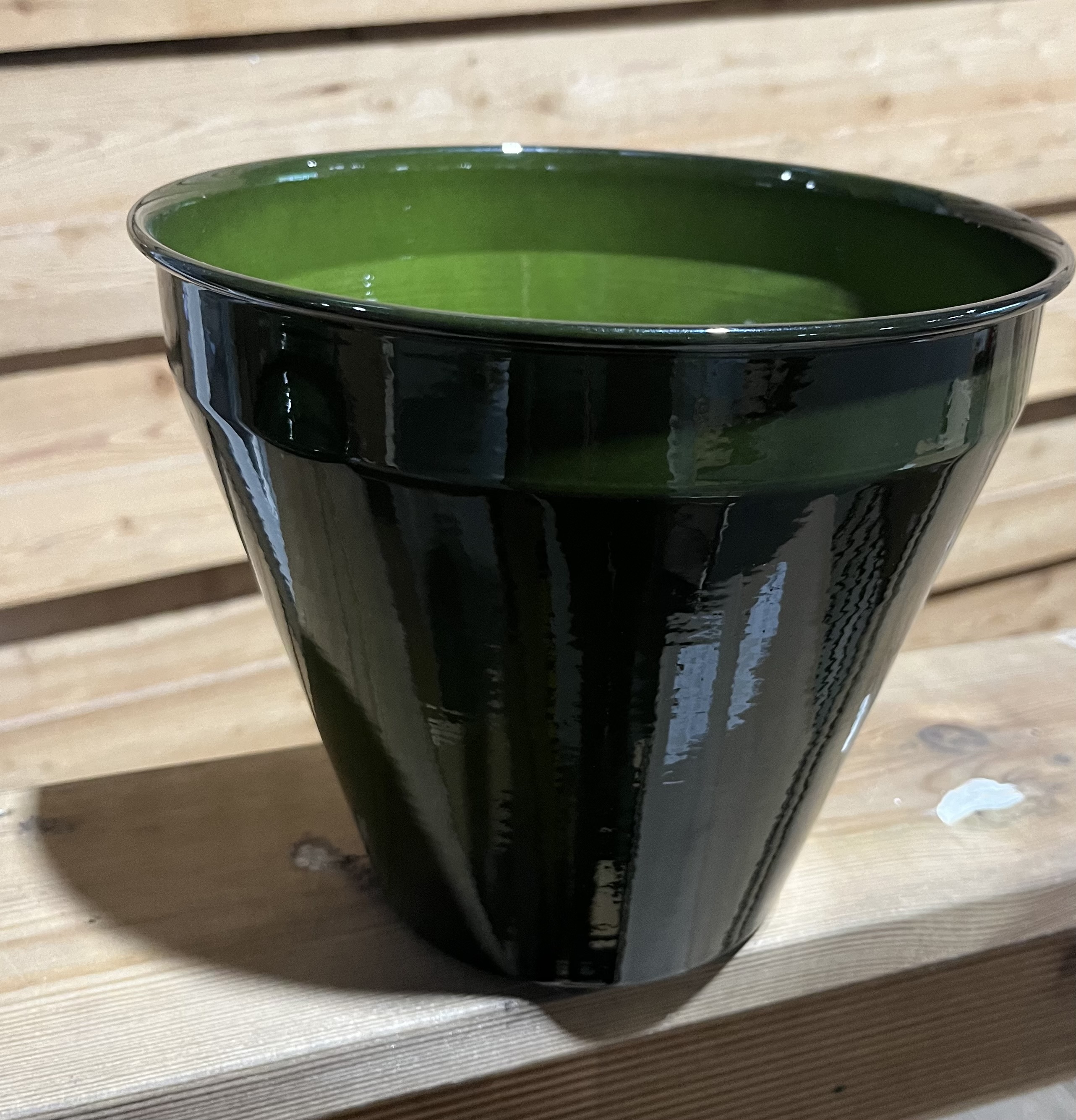 Den gröna metallkrukan Konical 20,5x20,5x18 står på trä med en bakgrund av träpanel.