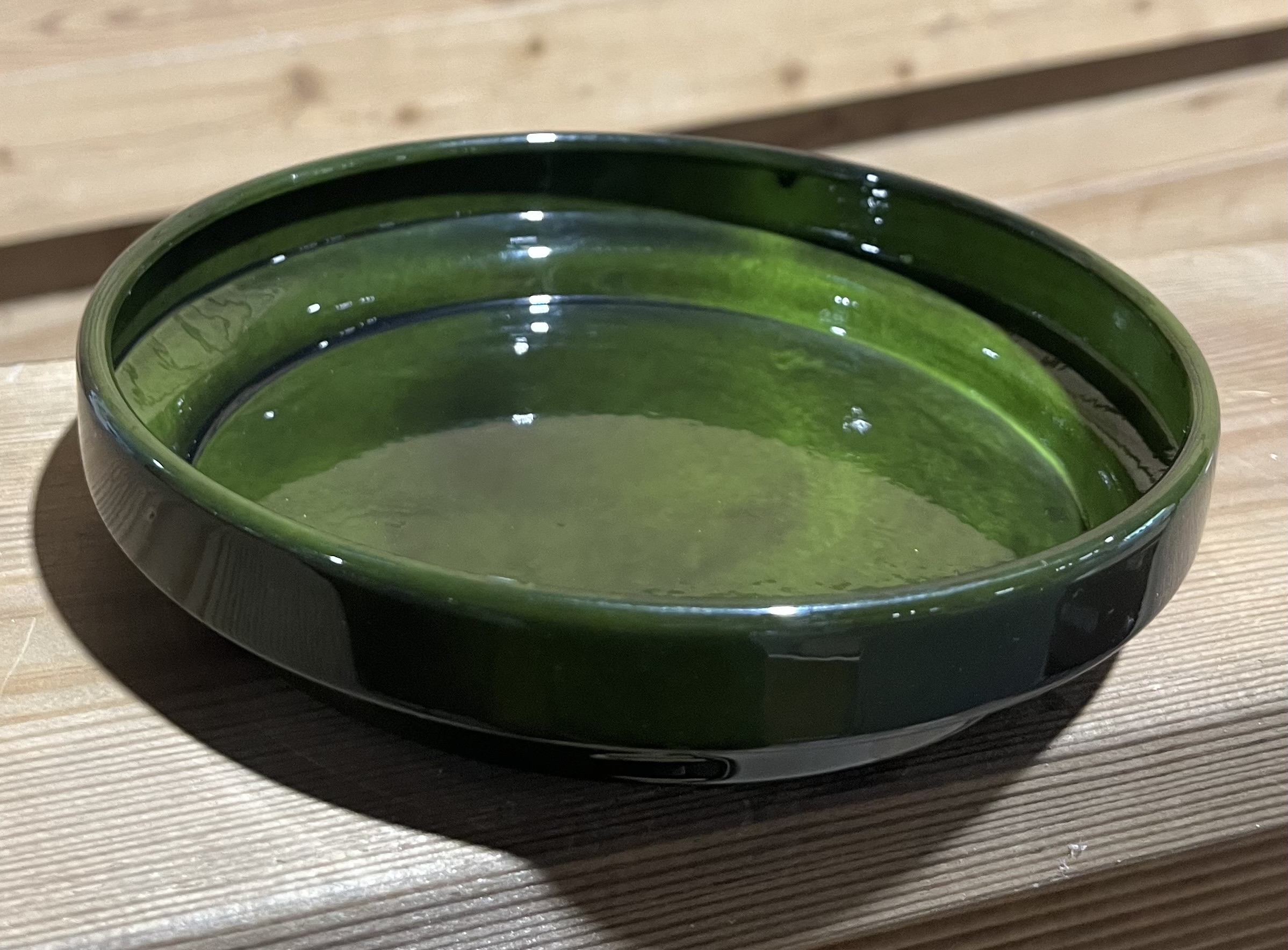 En Fat konical 12x12x2,5 grön glasskål med klar vätska står på en träyta.