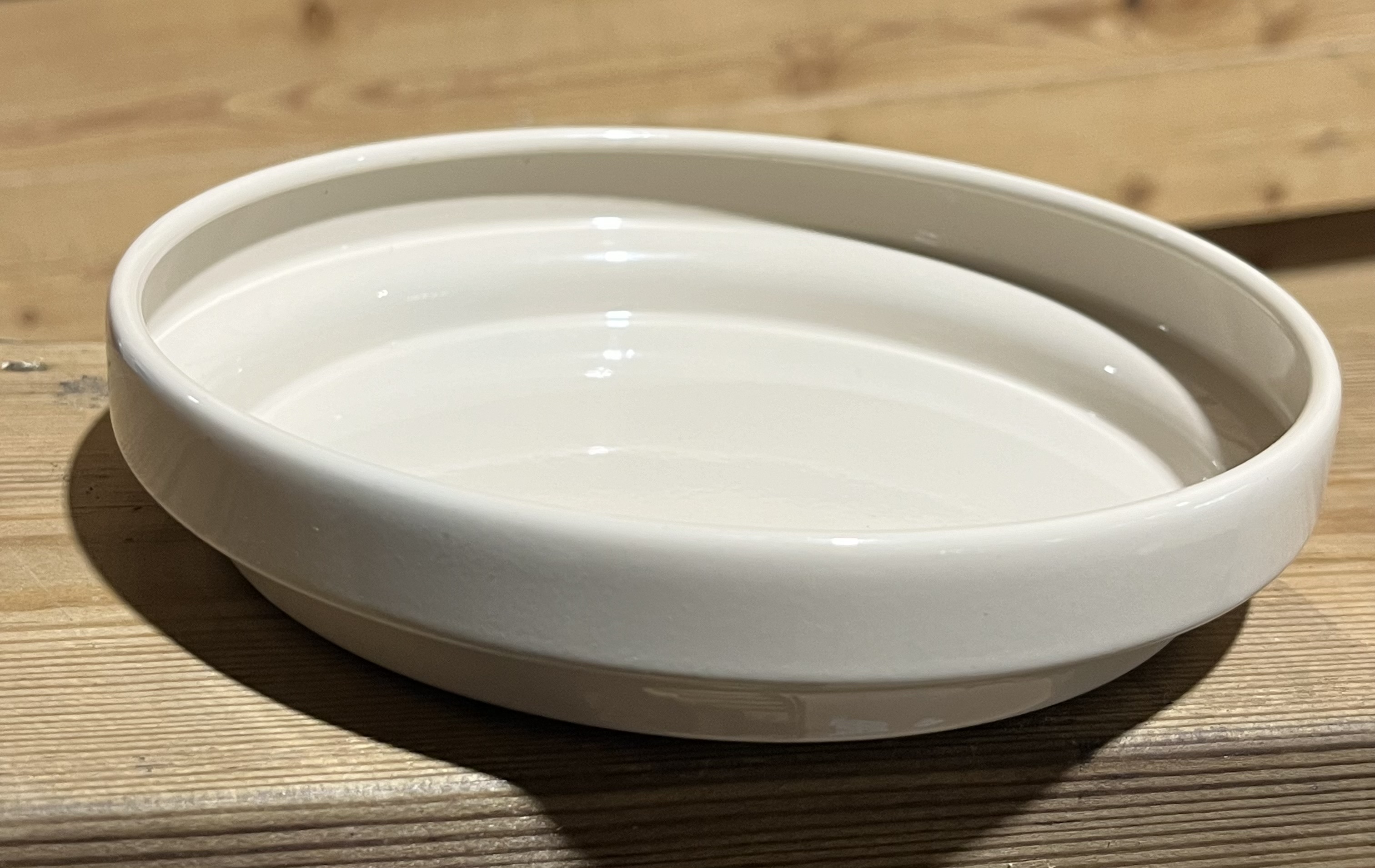 Fat konical 16,5x16,5x3,25 cream sitter på trä med en suddig träbakgrund.