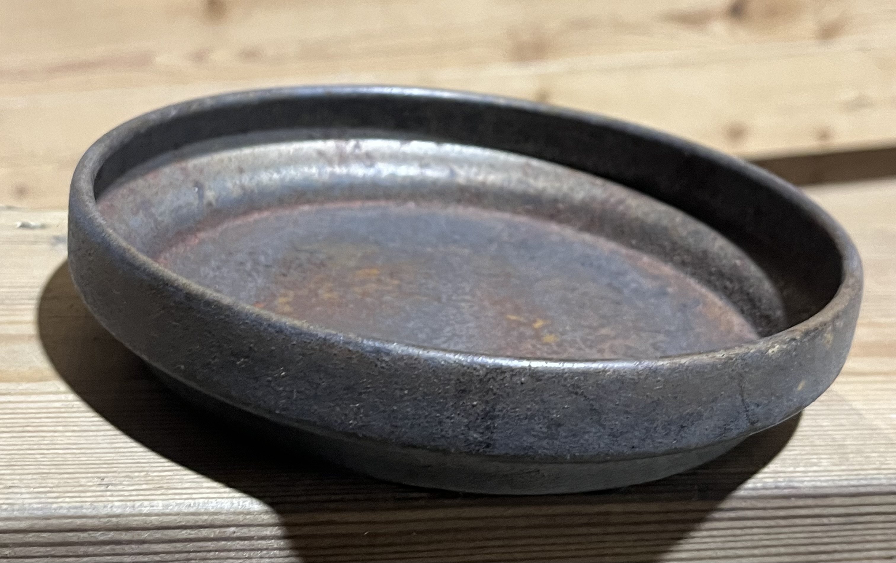 En Fat konical 16,5x16,5x3,25 rostskål sitter lutad på en träyta.