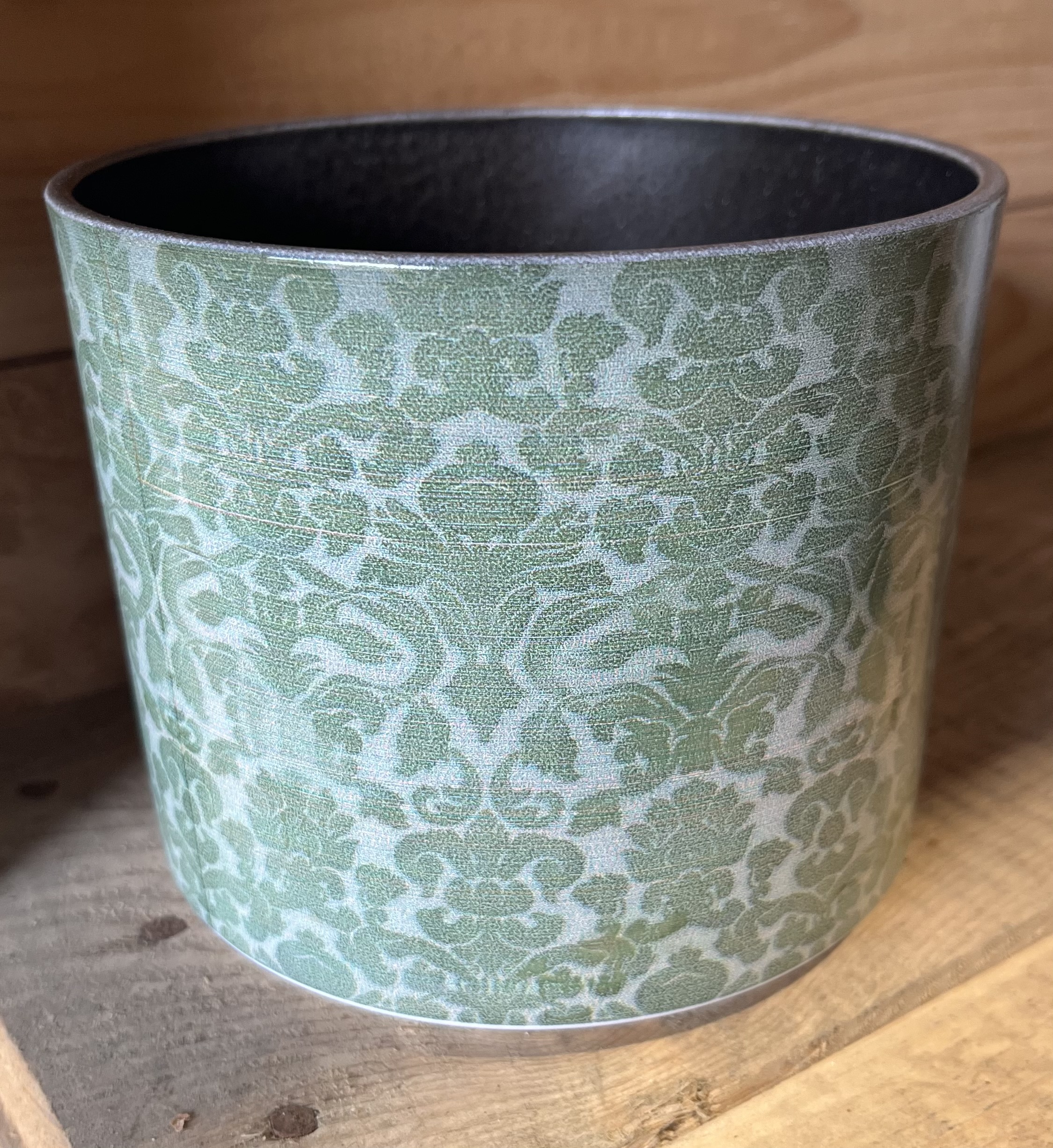 Prydnad grön keramikkruka, grön och vit, på träunderlag.