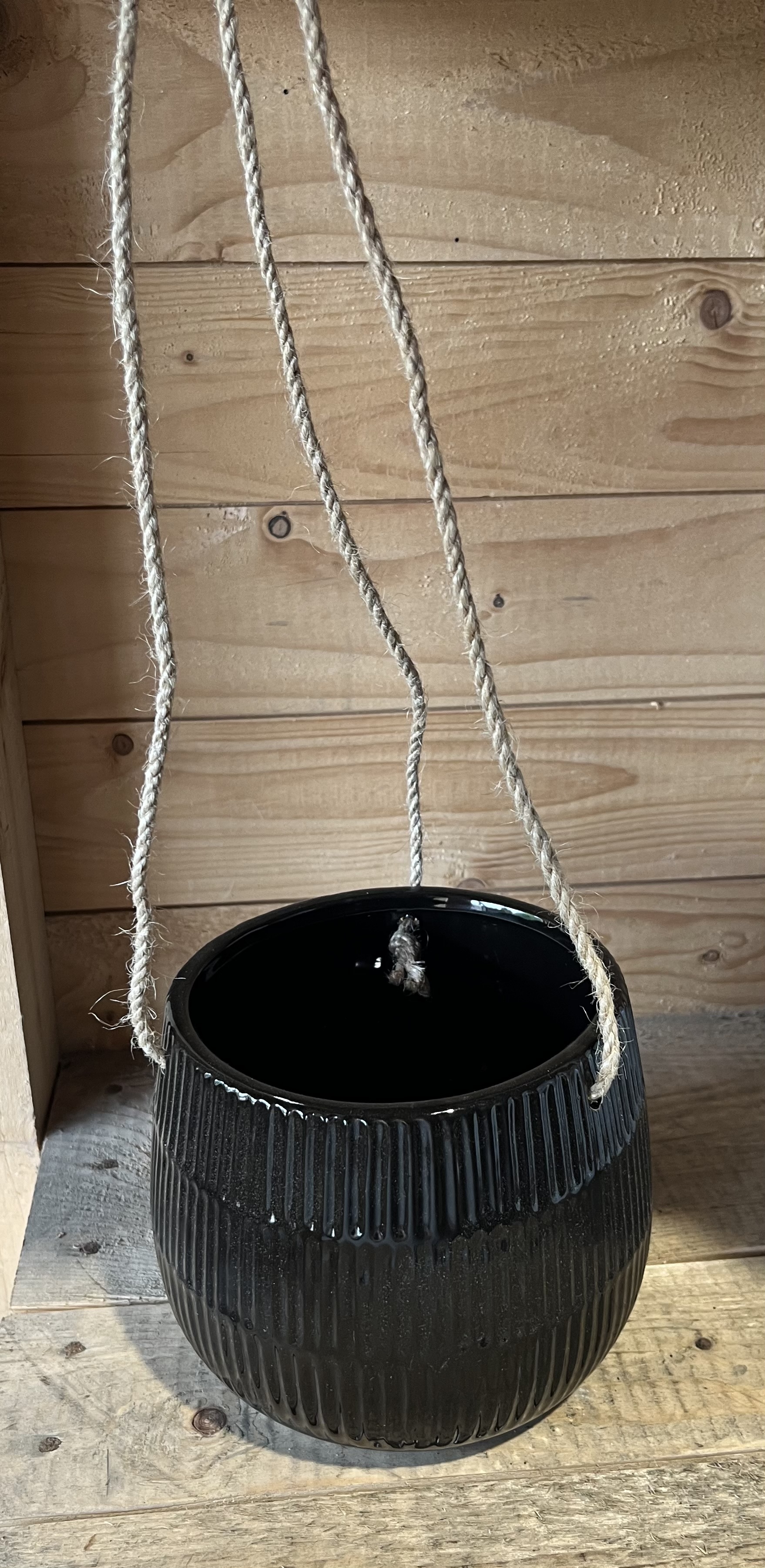 Keramikkruka ampel svart D12, hängande i rep, mot en bakgrund av trä.