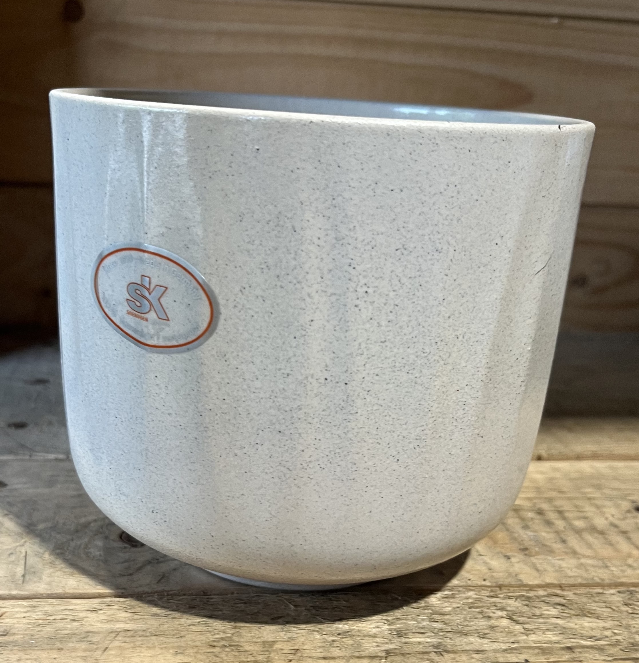 En vit keramikkopp med en liten orange Bagua cream-logotyp, placerad på en träyta.