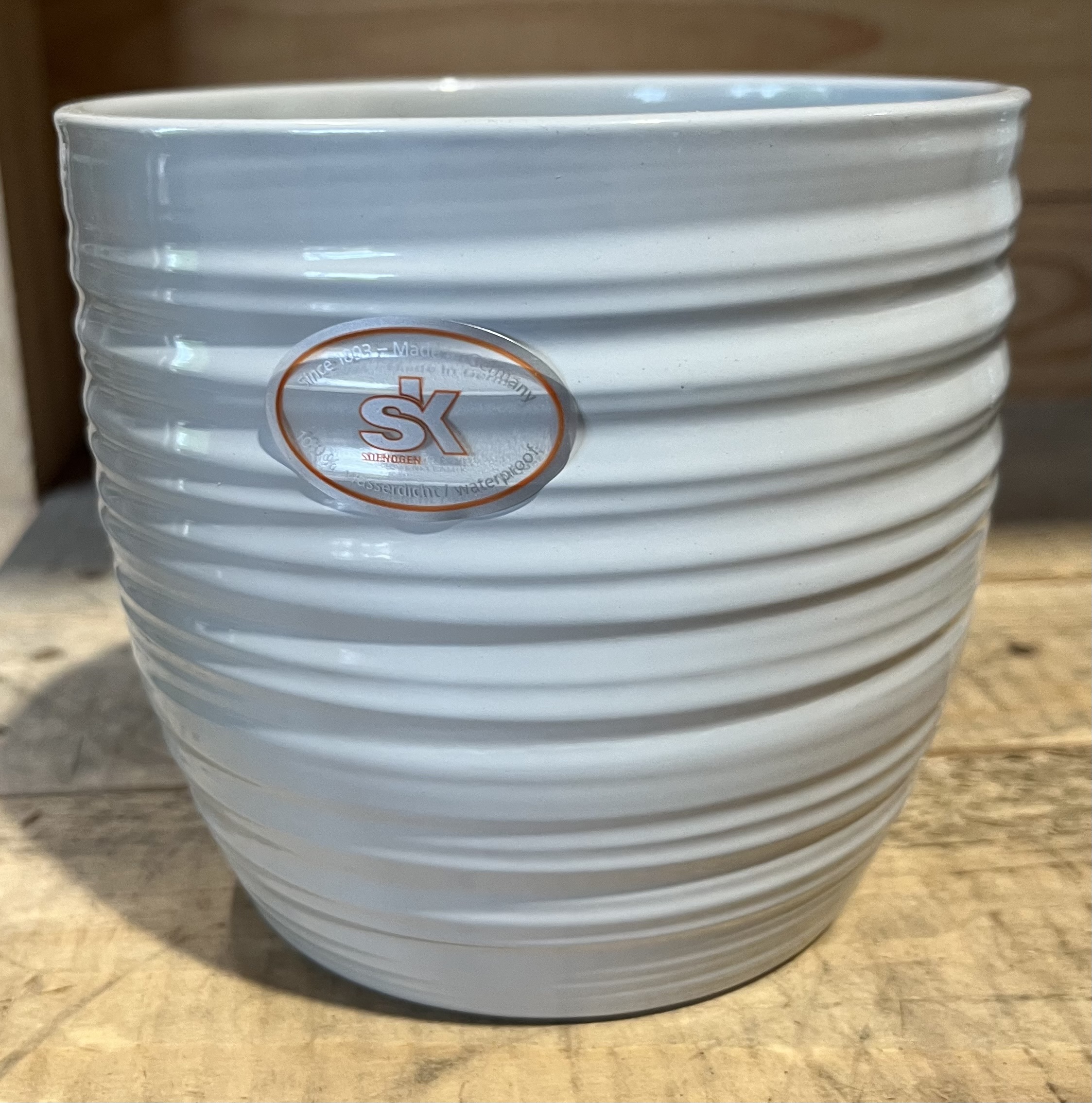 Bergamo hellgrau keramikkruka med horisontella räfflor och SK-logotyp på en träyta.