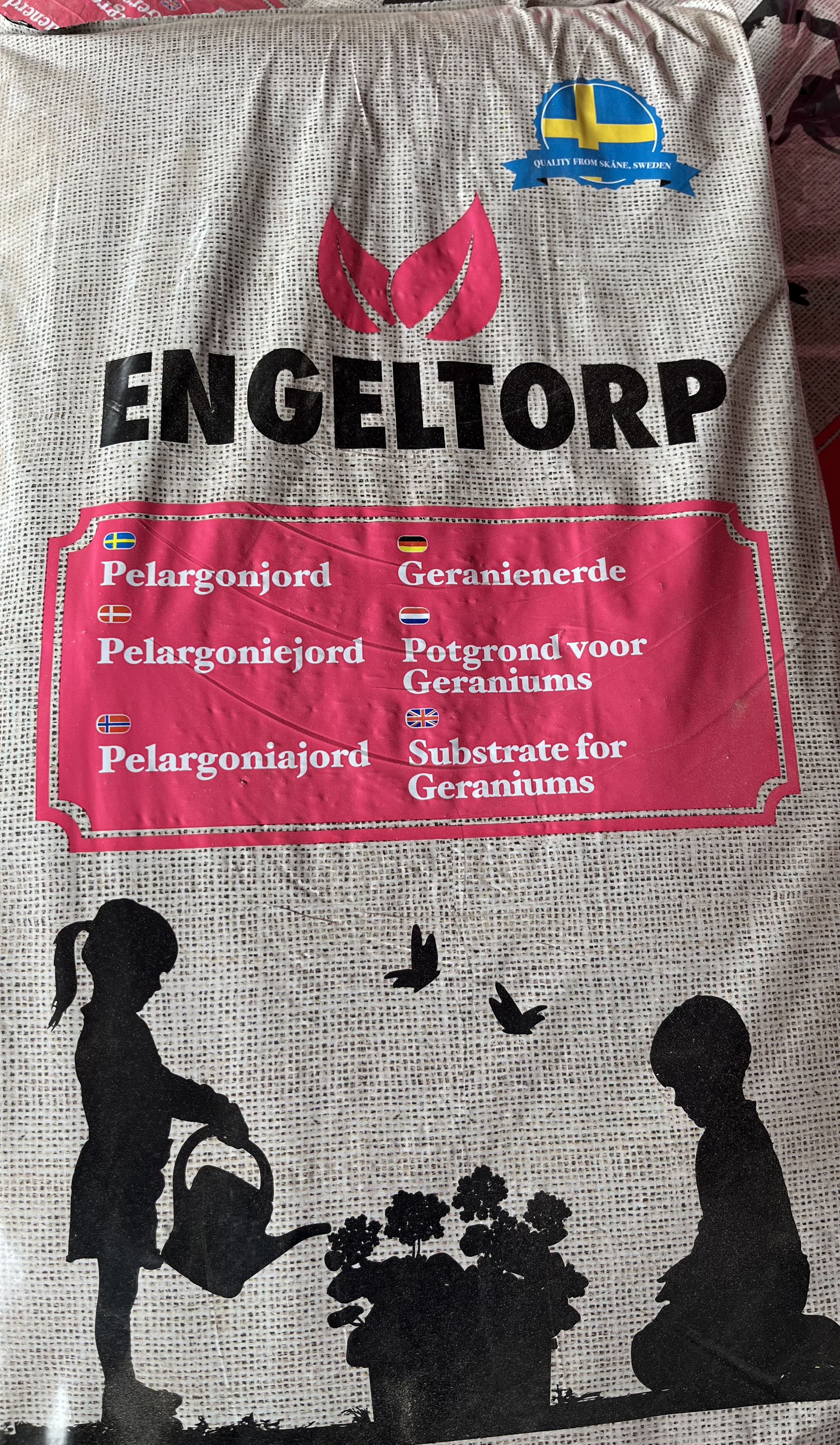 Påse med Pelargon jord 20 l med silhuetter av barn som vattnar trädgårdsväxter.