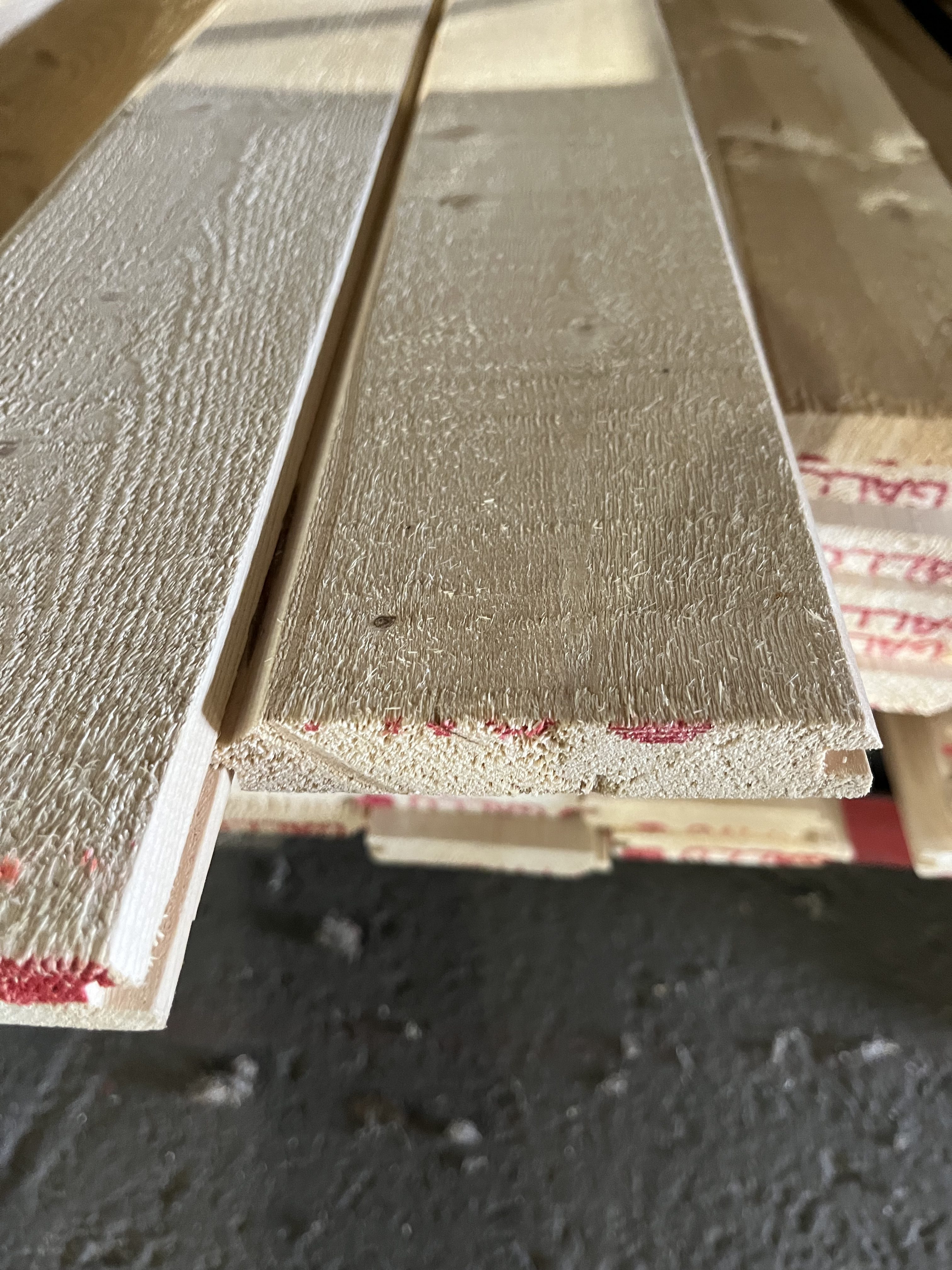 Närbild av Hyvlad dubbelfas 21*120 brädor med not och fjäder, staplade på betonggolv.