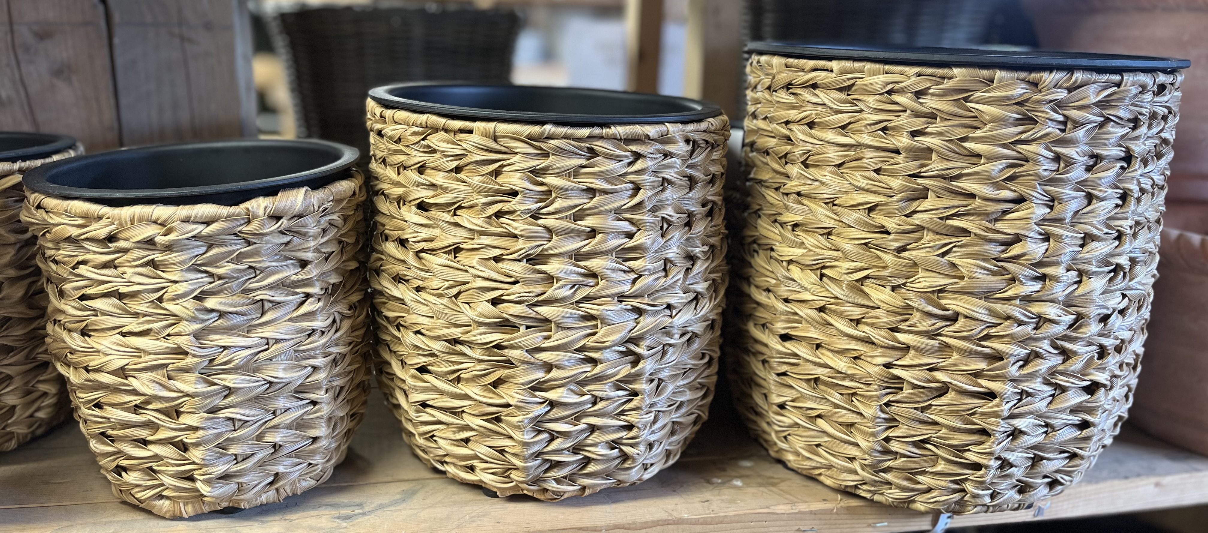 Tre korgar D21 i polyrattan med svart insida på en hylla av trä.