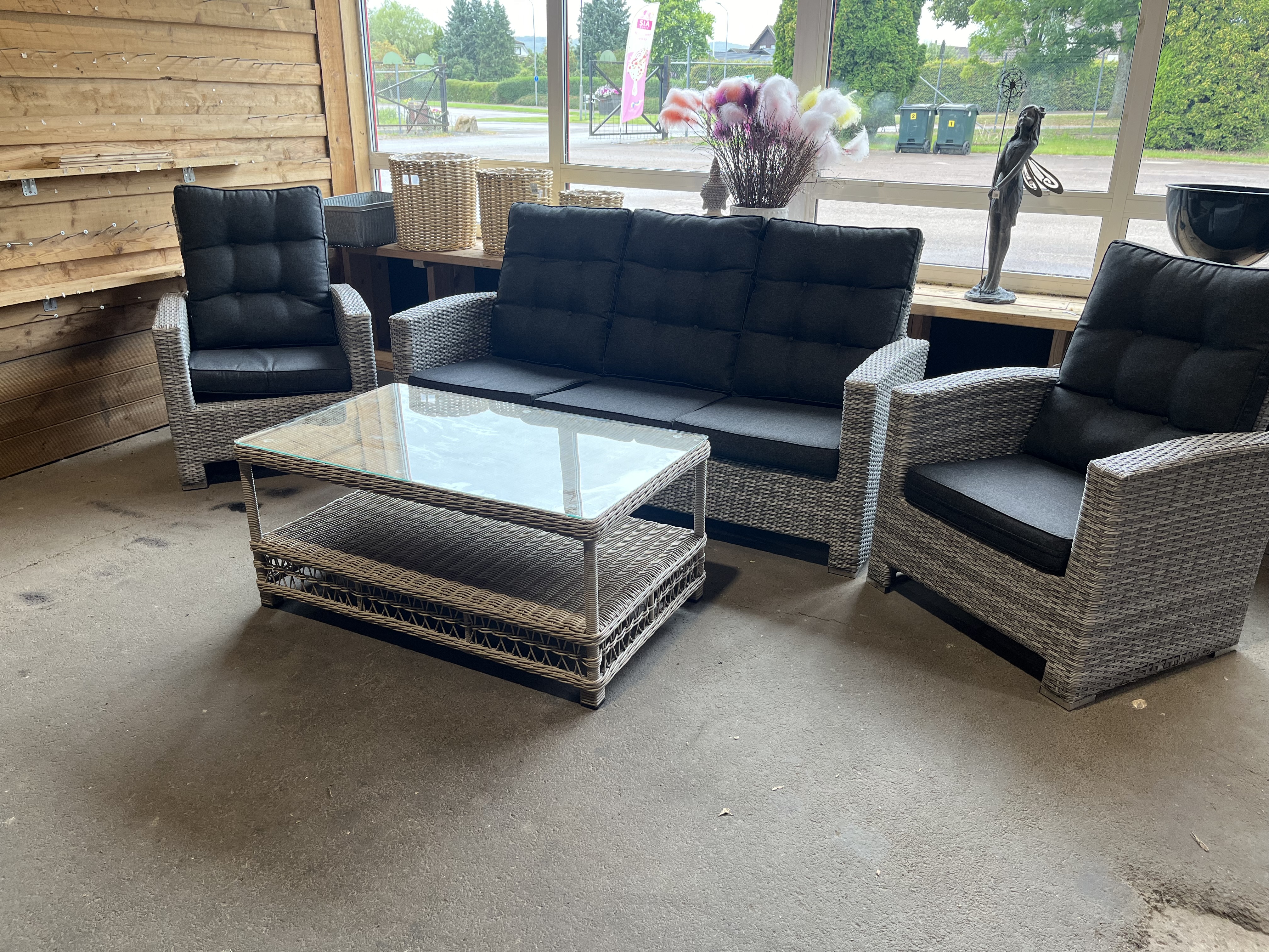 Utemöbelset 6: Grå uteplats i rotting med bord med glasskiva vid stora fönster.