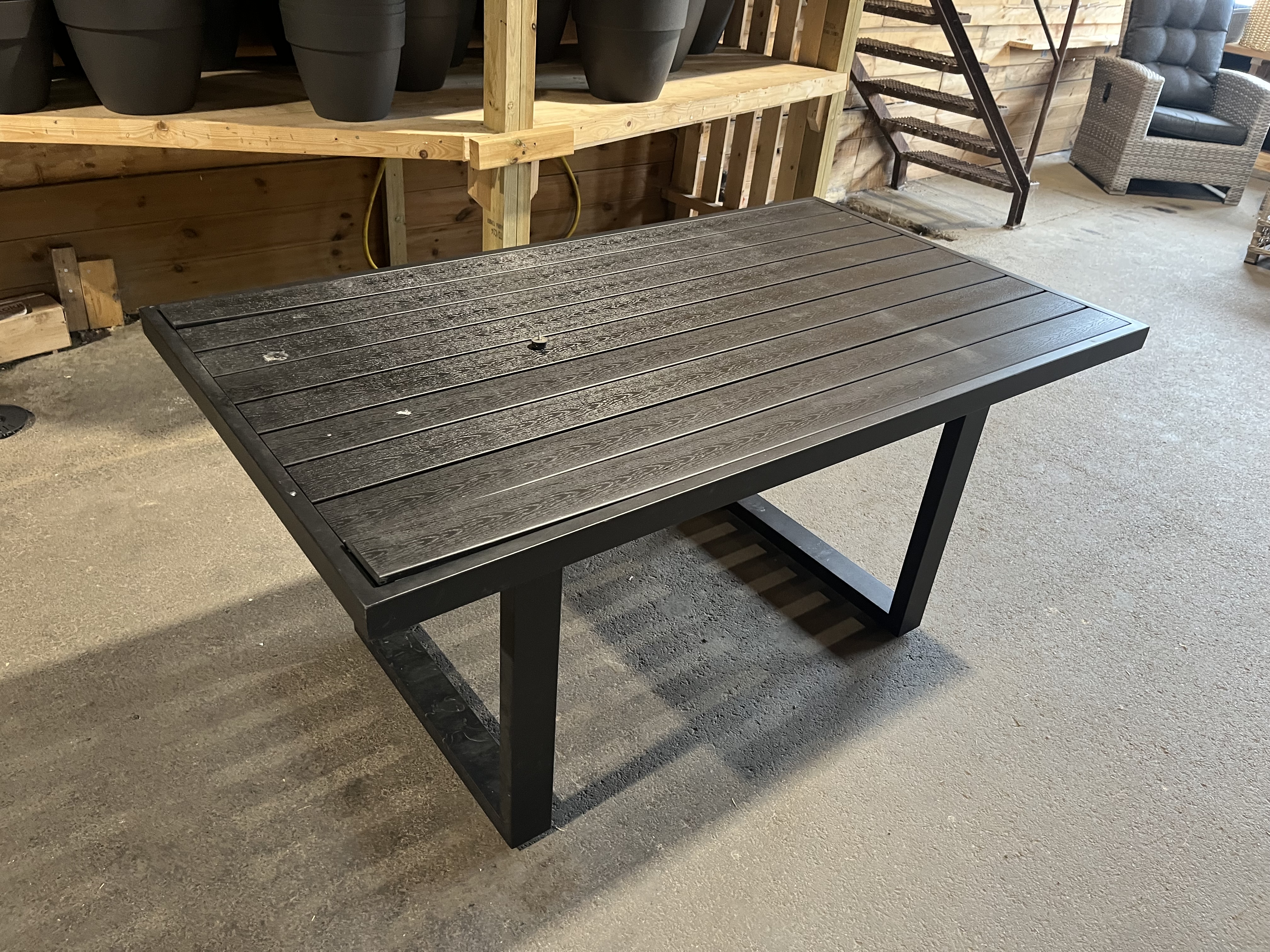 Bord 2: Ett svart rektangulärt utomhusbord på ett betonggolv i ett trärum.