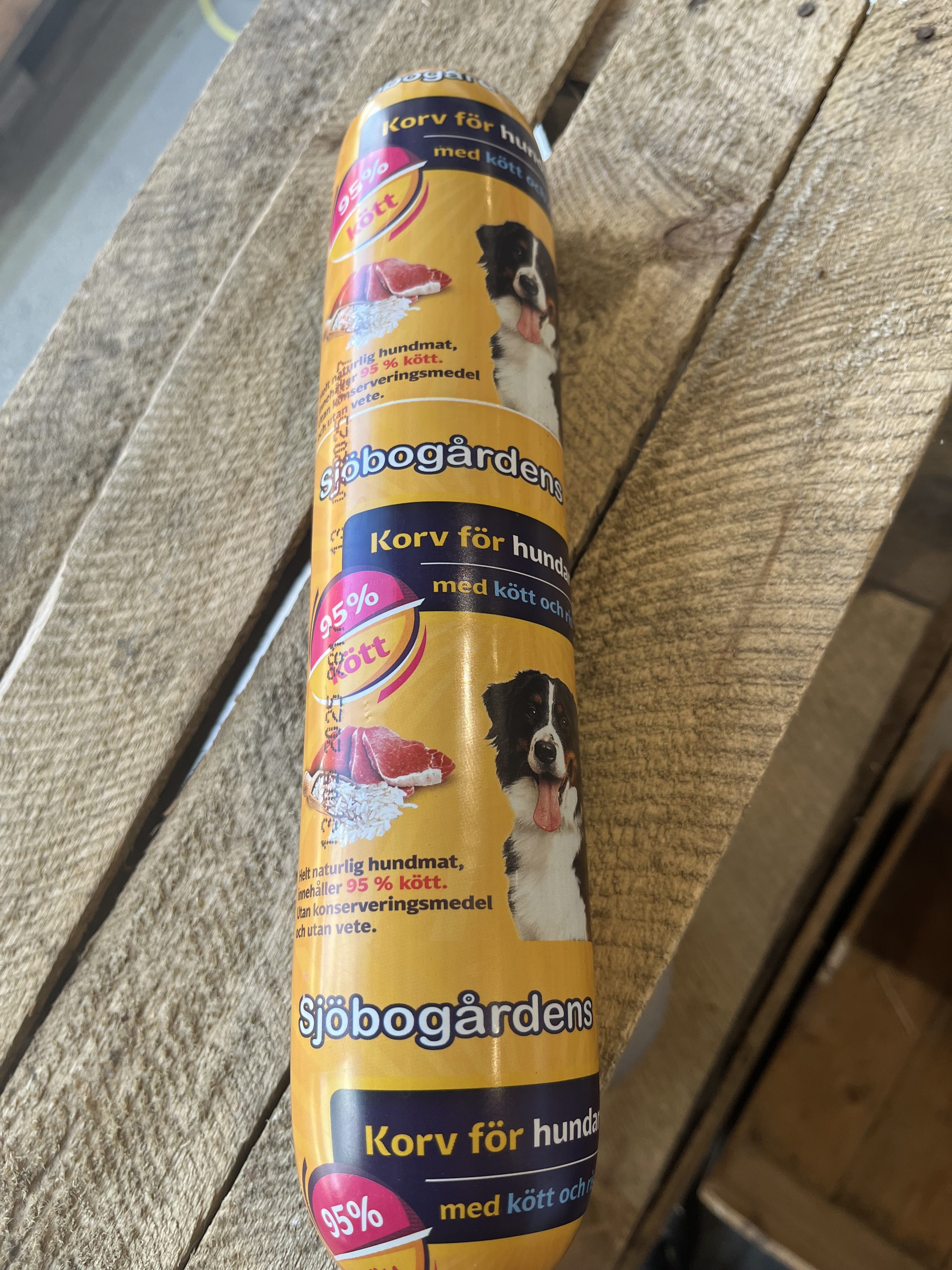 Gul tub med Hundmat Köttkorv med ris 1000g på en träyta.